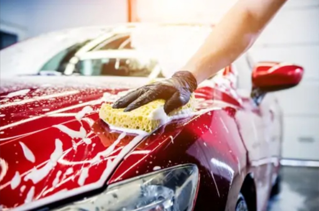 Hand washing a red car with sponge and foam